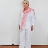 Woman wearing a pink scarf and white outfit against a plain background