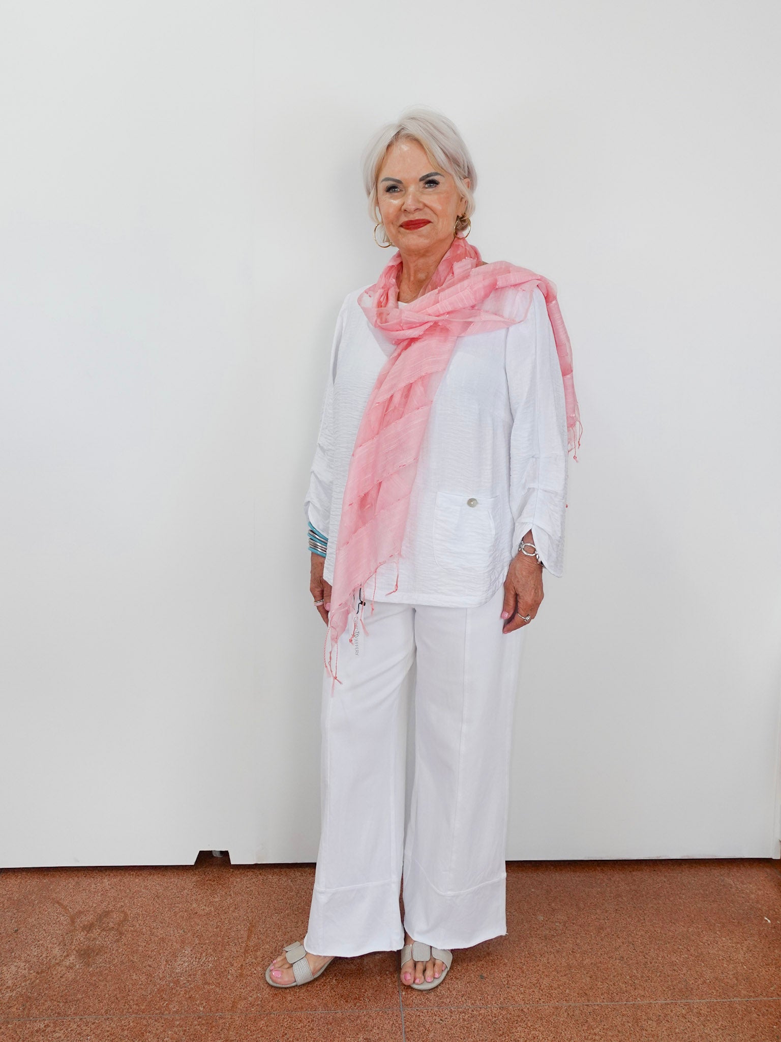 Woman wearing a pink scarf and white outfit against a plain background