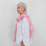Woman wearing a pink scarf and white outfit against a plain background