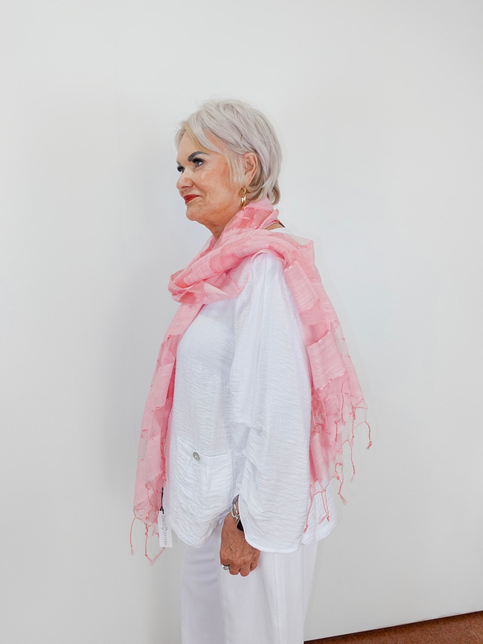 Woman wearing a pink scarf and white outfit against a plain background