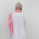 Person wearing a white shirt and light pink scarf against a plain background