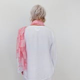 Person wearing a white shirt and light pink scarf against a plain background