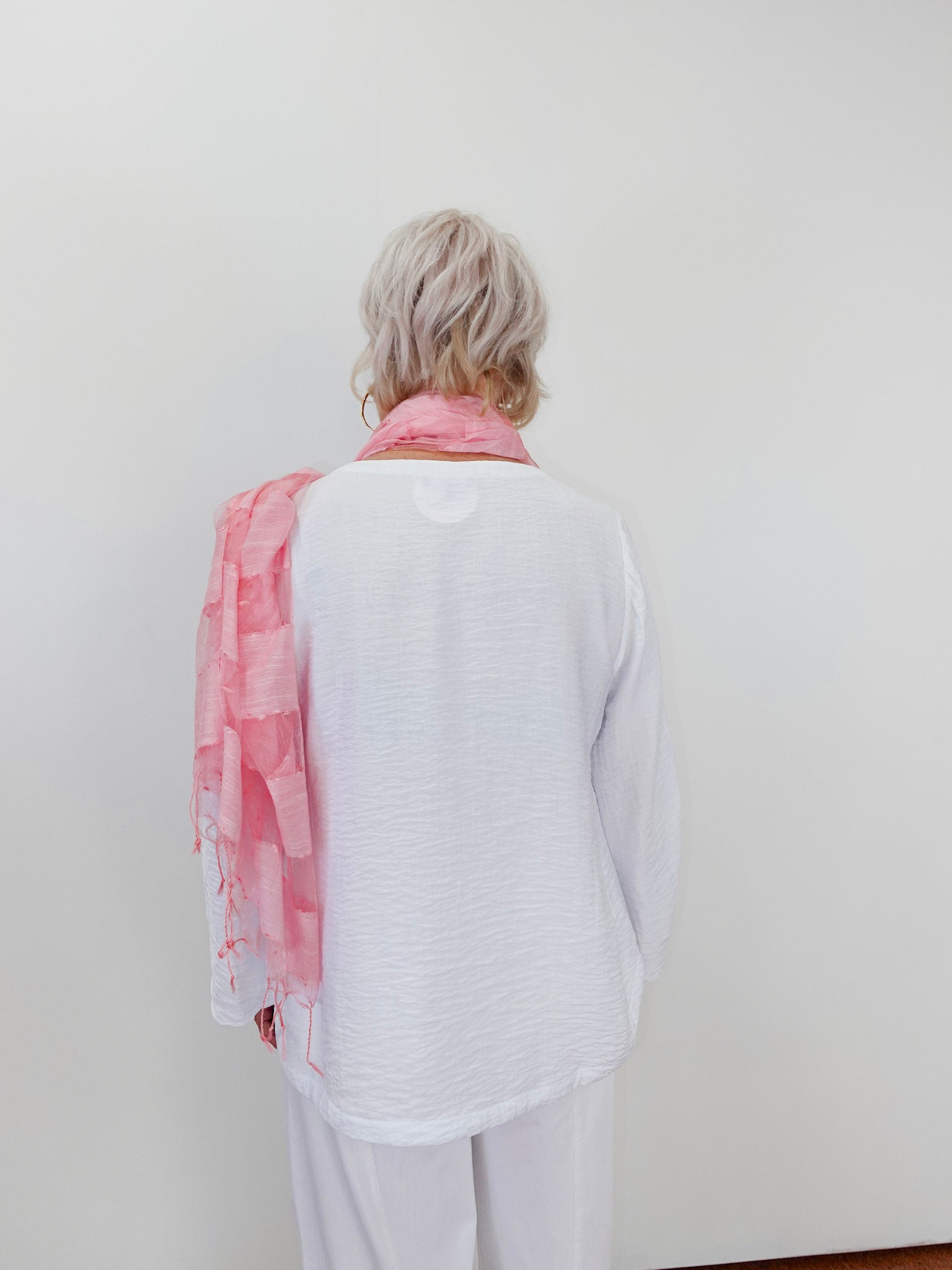 Person wearing a white shirt and light pink scarf against a plain background