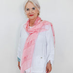 Woman wearing a pink scarf and white outfit against a plain background