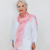 Woman wearing a pink scarf and white outfit against a plain background