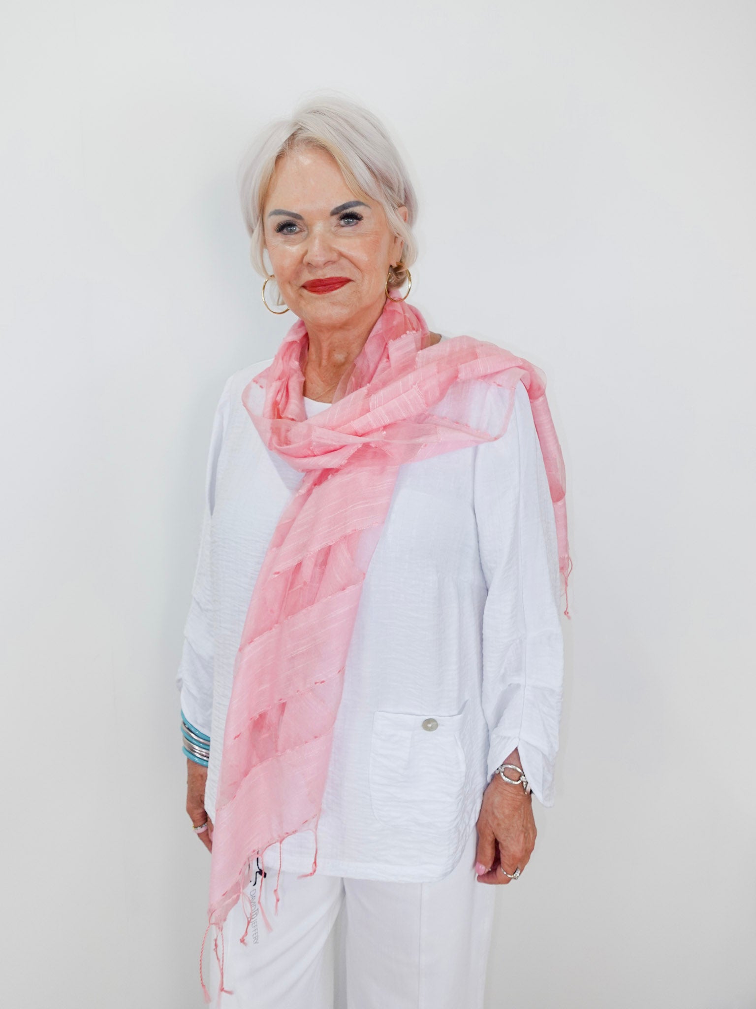 Woman wearing a pink scarf and white outfit against a plain background