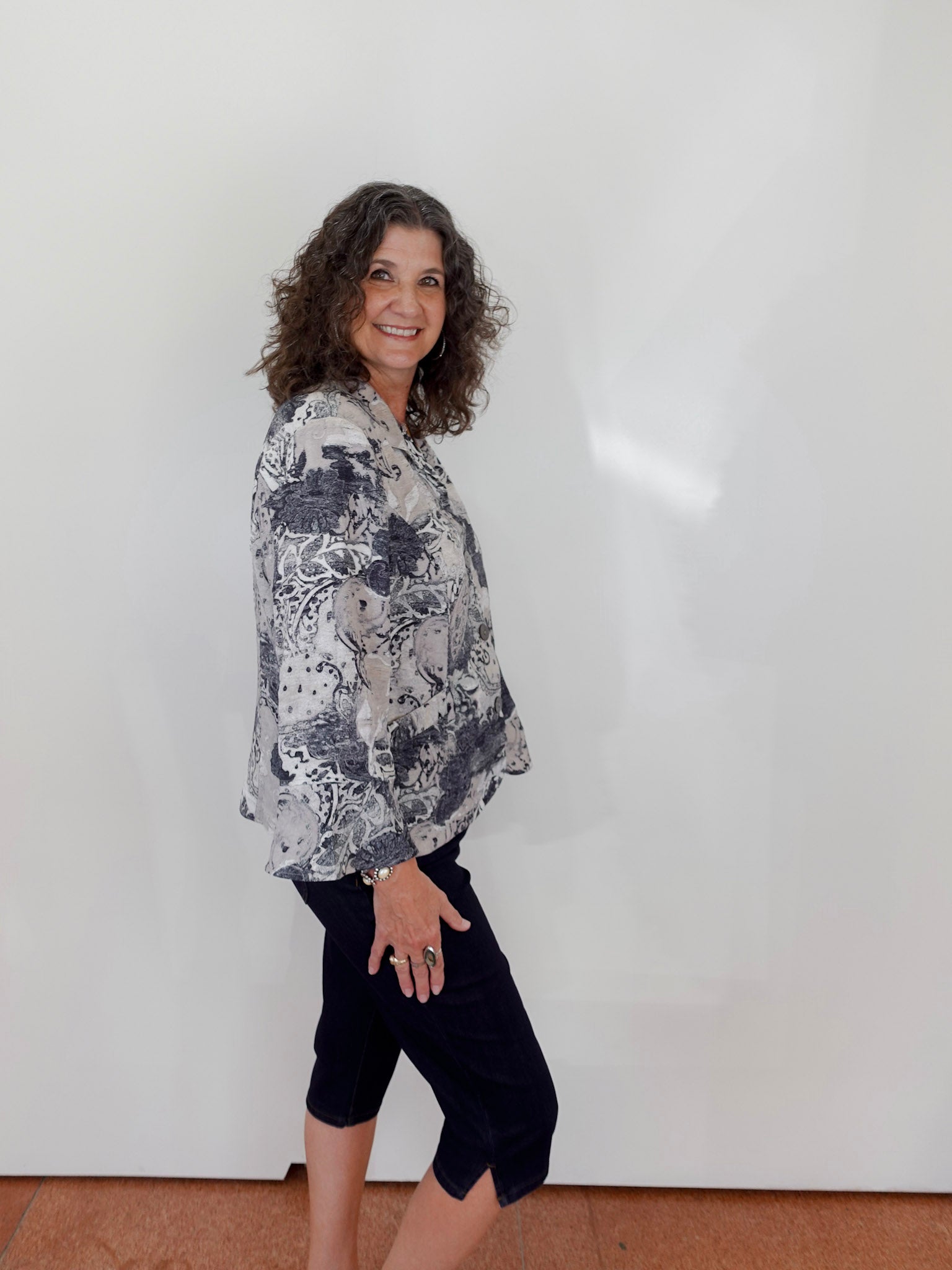 Woman wearing a floral blouse and black pants against a white wall