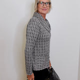 Woman wearing a patterned sweater and glasses against a white wall