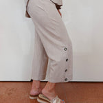 Person wearing a light-colored outfit with wide-leg pants and sandals on a plain background
