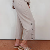 Person wearing a light-colored outfit with wide-leg pants and sandals on a plain background