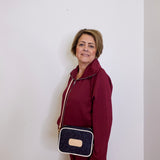 Woman in a burgundy outfit holding a navy blue handbag with a beige strap against a white background