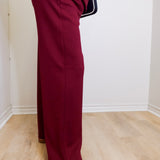 Person wearing burgundy pants and white sneakers with black stripes on a light wooden floor.