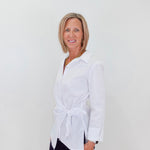 Woman wearing a white blouse with a tie waist against a plain background