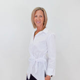 Woman wearing a white blouse with a tie waist against a plain background