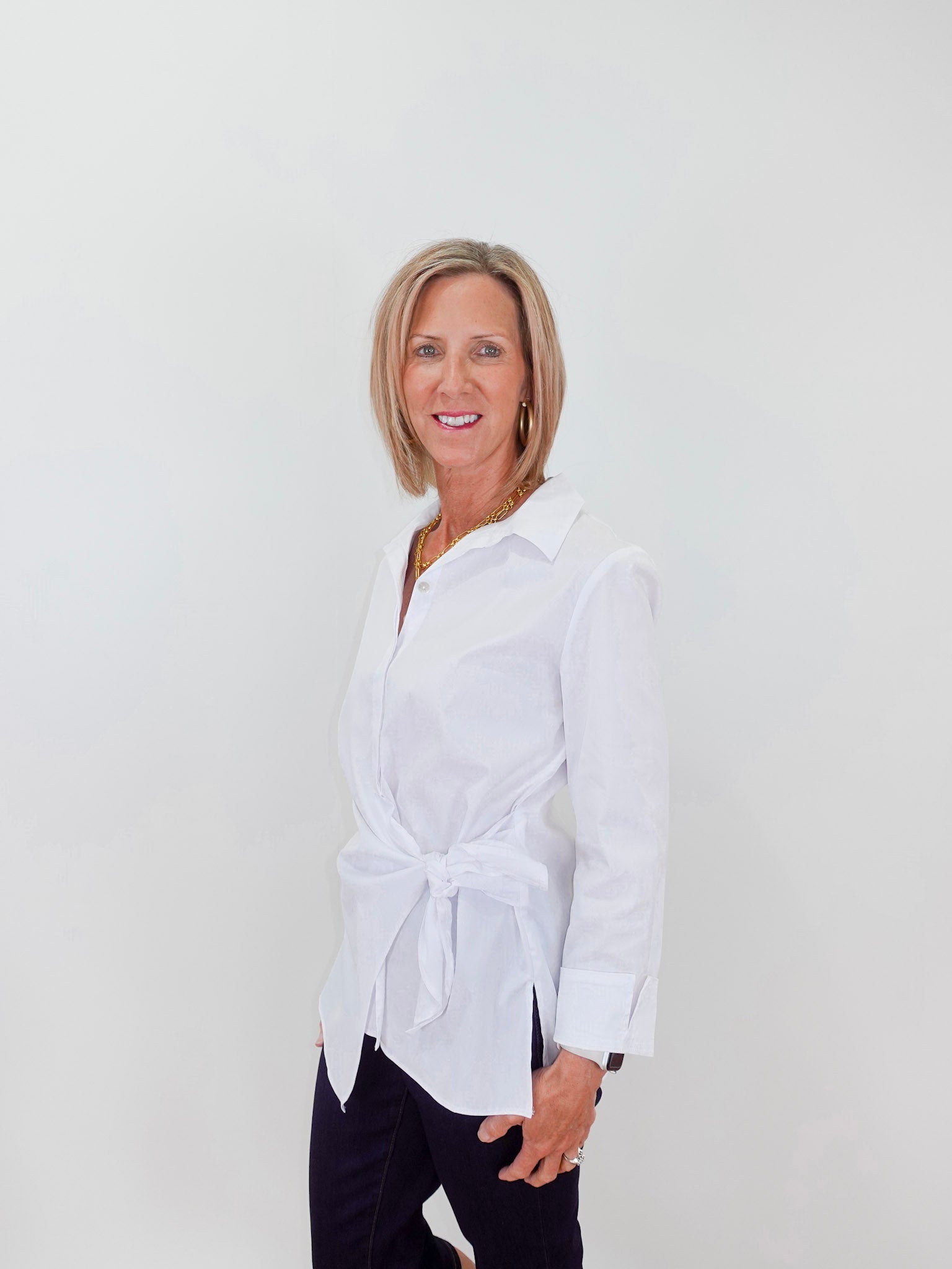 Woman wearing a white blouse with a tie waist against a plain background