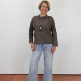 A woman modeling a textured brown knit sweater and light-wash wide-leg jeans against a plain white wall.