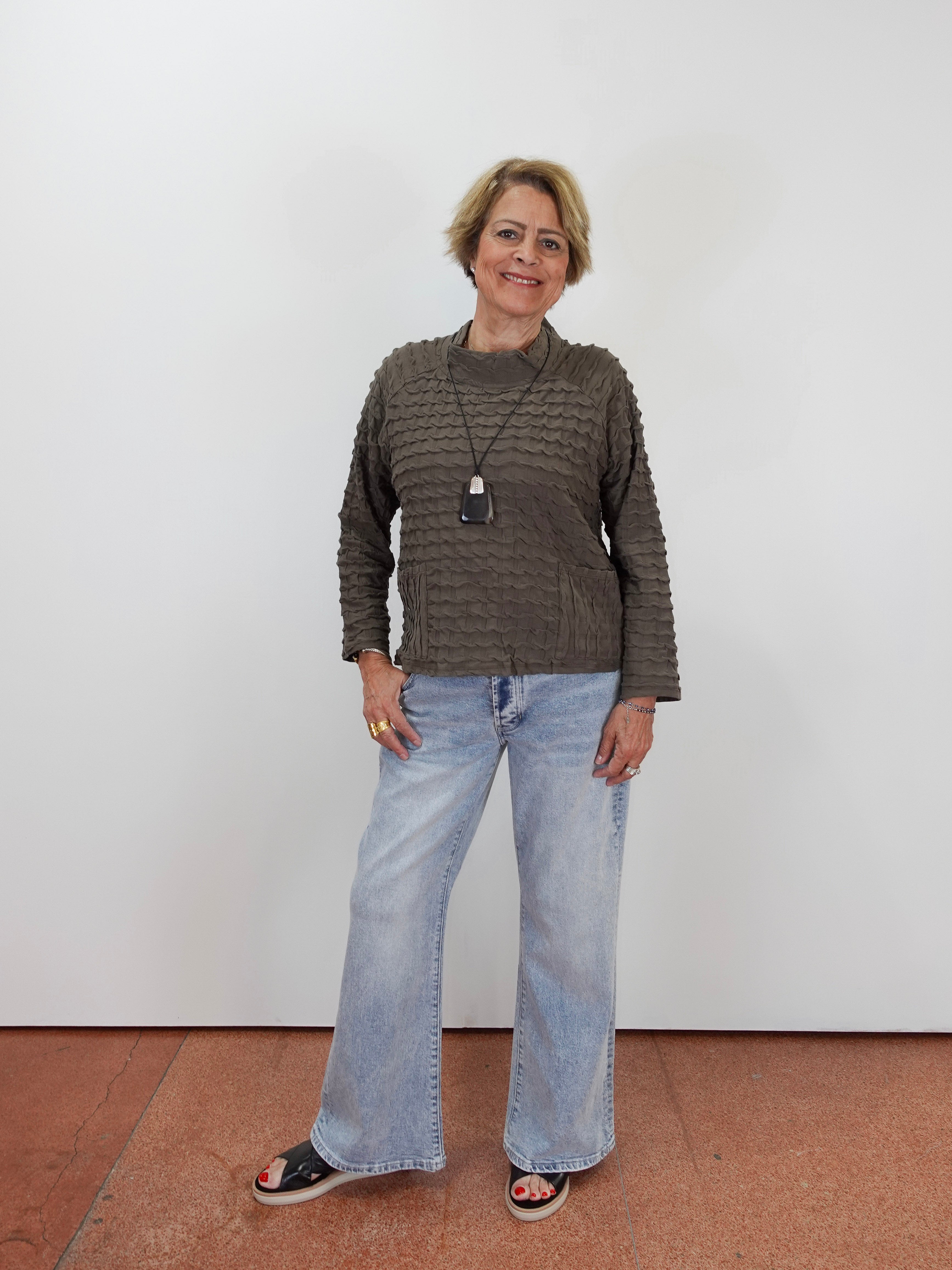 A woman modeling a textured brown knit sweater and light-wash wide-leg jeans against a plain white wall.