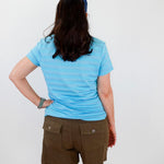 Person wearing a blue striped shirt and brown shorts against a white wall.