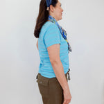 Woman wearing a blue shirt and brown shorts with a headband, standing against a white wall.