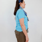 Woman wearing a blue shirt and brown shorts with a headband, standing against a white wall.
