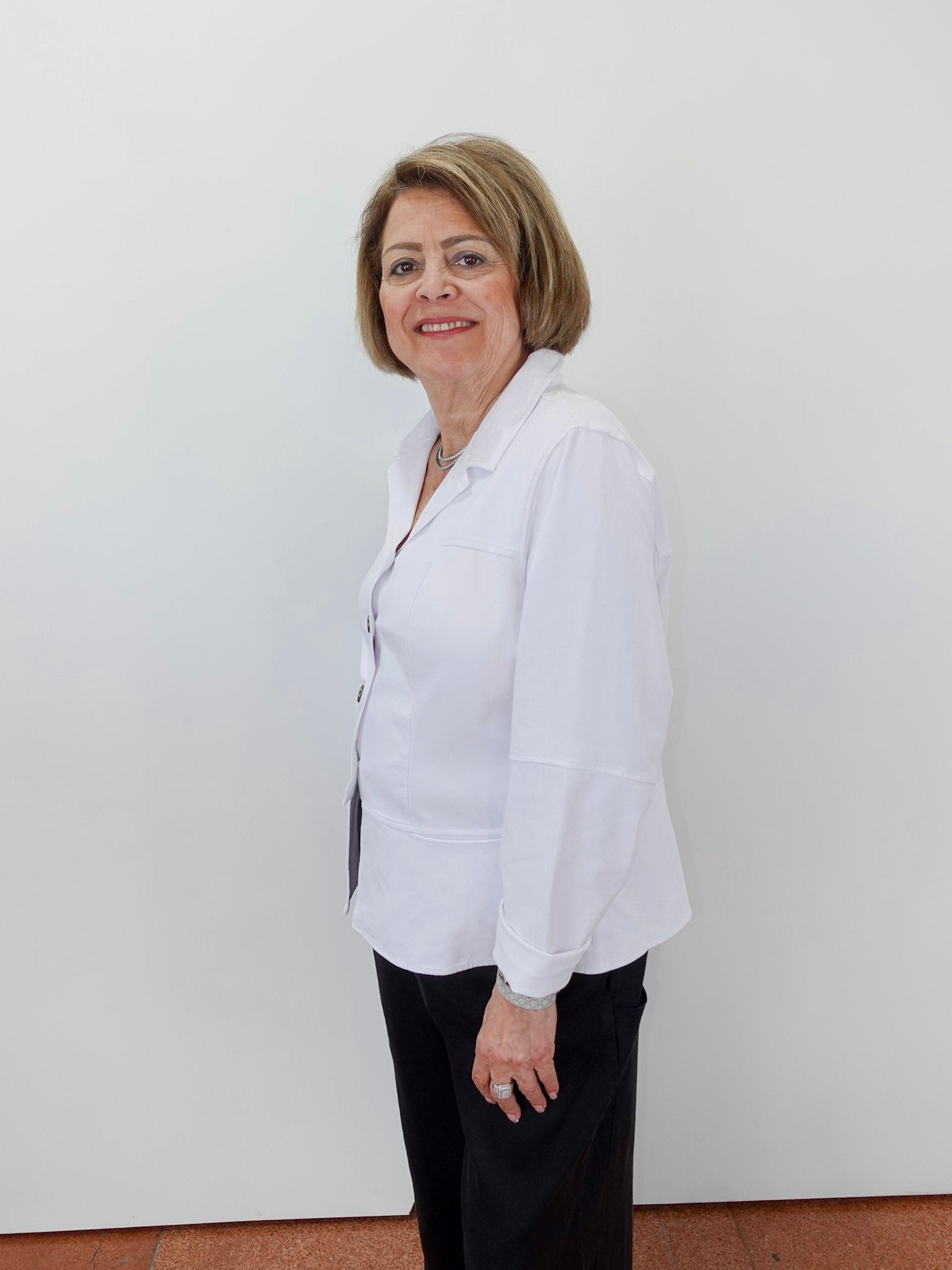 Woman wearing a white blouse and black pants against a plain background