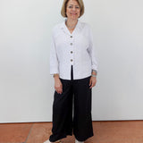 Woman wearing a white blouse and black pants standing against a plain background