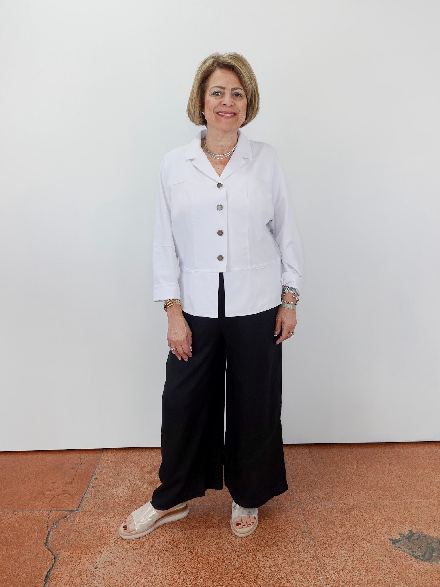 Woman wearing a white blouse and black pants standing against a plain background