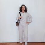 Woman in a light gray suit standing against a white wall.