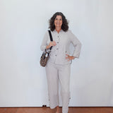Woman in a light gray suit standing against a white wall.