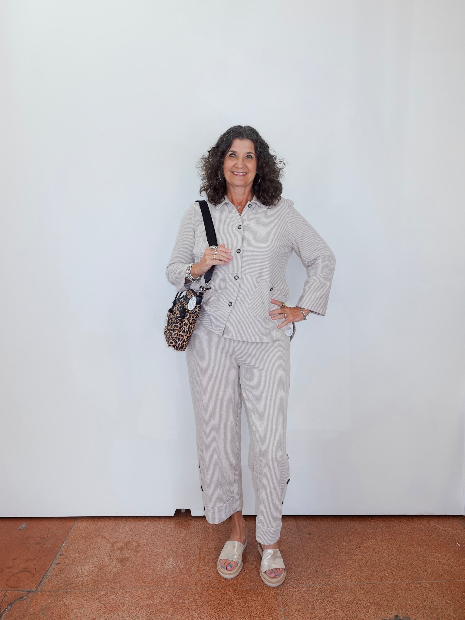 Woman in a light gray suit standing against a white wall.