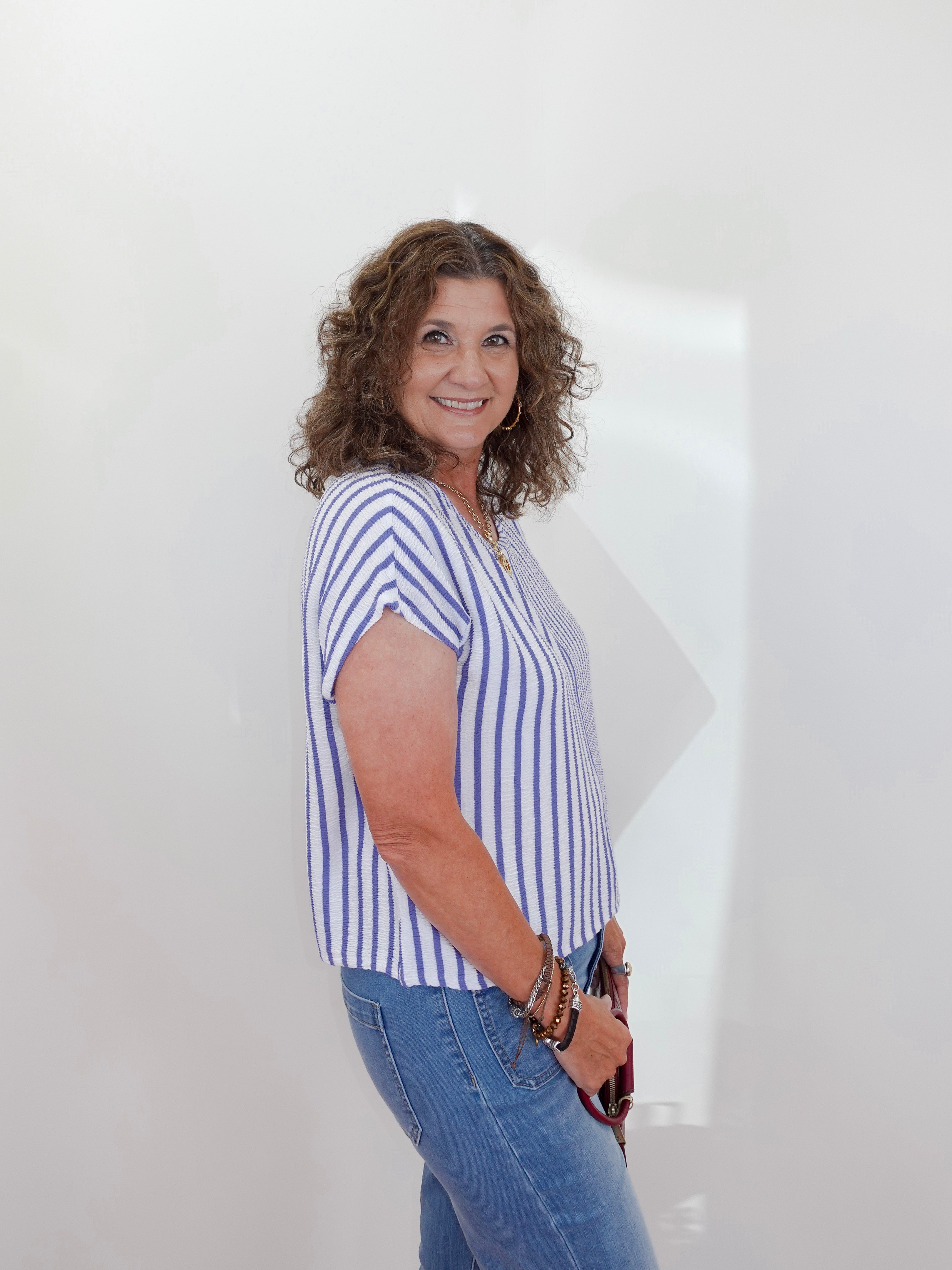 Woman wearing a striped shirt and jeans against a white wall