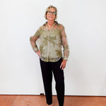 Person wearing a patterned shirt and black pants standing against a white wall.