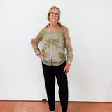 Person wearing a patterned shirt and black pants standing against a white wall.