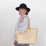 Person wearing a black hat and holding a beige tote bag against a white background