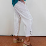 Person wearing white pants and brown sandals on a plain background
