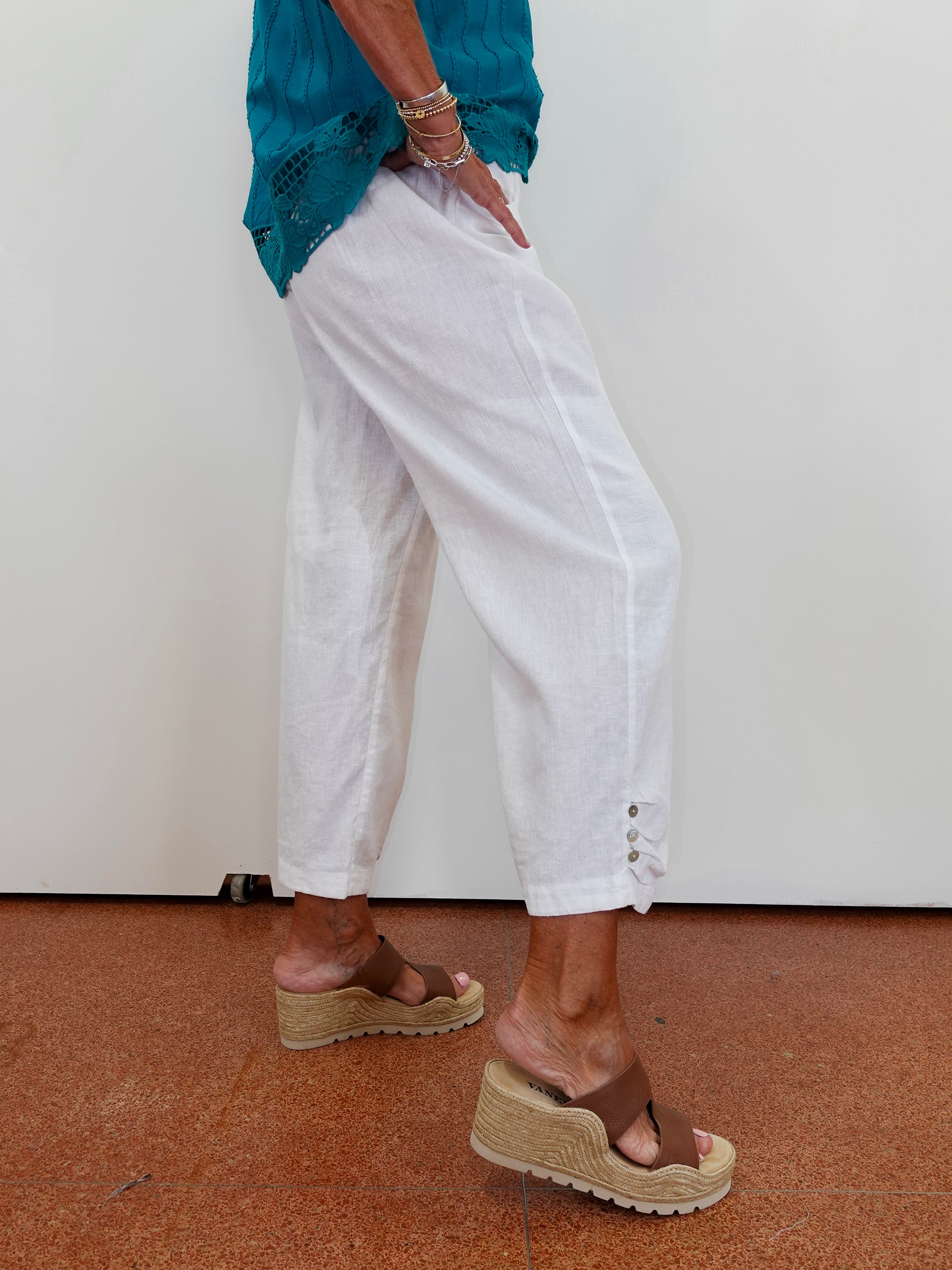 Person wearing white pants and brown sandals on a plain background