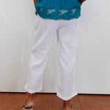 Person wearing a teal top and white pants standing against a white wall.