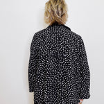Person wearing a black polka dot jacket against a white background