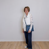 Woman wearing a white vest, patterned shirt, blue jeans, and white sneakers against a plain white wall.