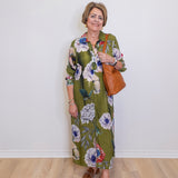 Woman wearing a floral dress with a brown bag against a white wall.
