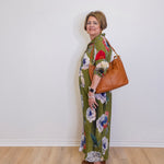 Woman wearing a floral dress with a brown bag against a white wall