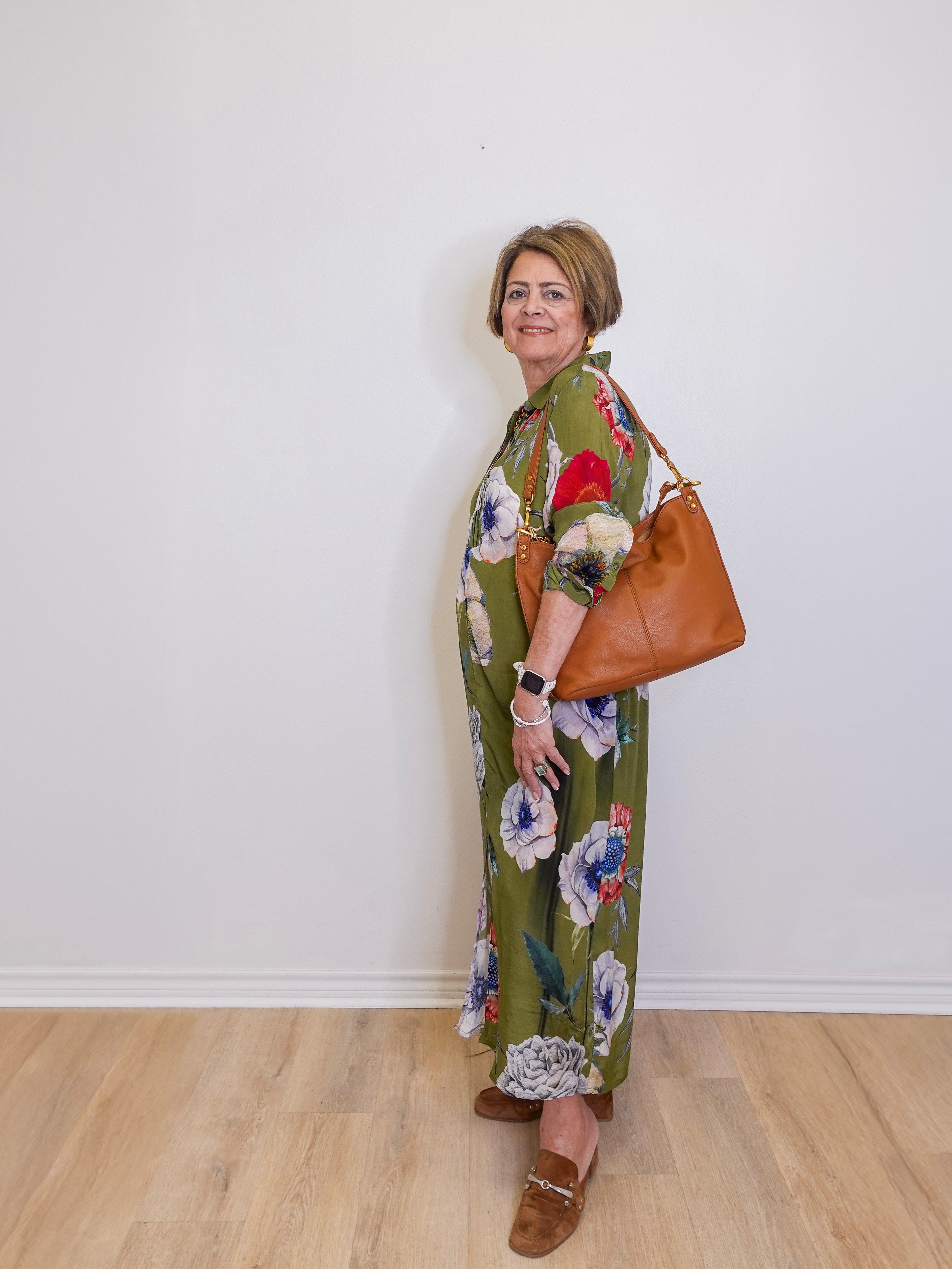 Woman wearing a floral dress with a brown bag against a white wall
