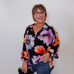 Woman wearing a colorful floral blouse against a white wall