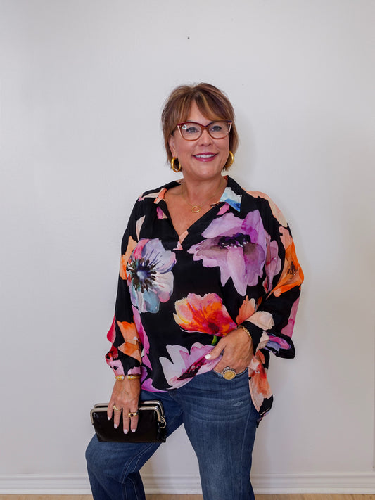 Woman wearing a colorful floral blouse against a white wall