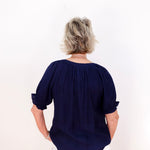 Person wearing a navy blue blouse with rolled-up sleeves on a white background