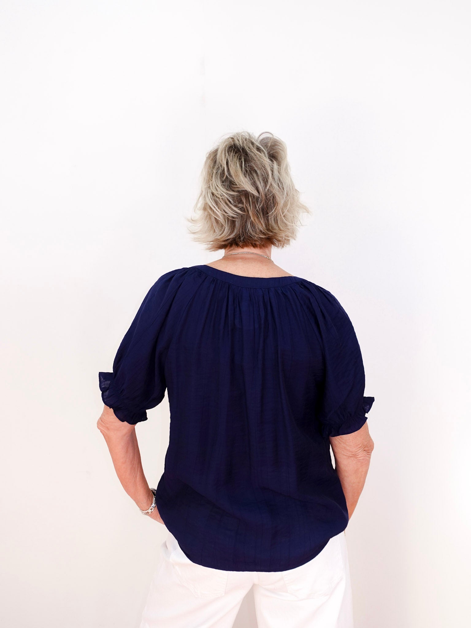 Person wearing a navy blue blouse with rolled-up sleeves on a white background