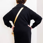 Person wearing a black dress with a gold strap over a white background