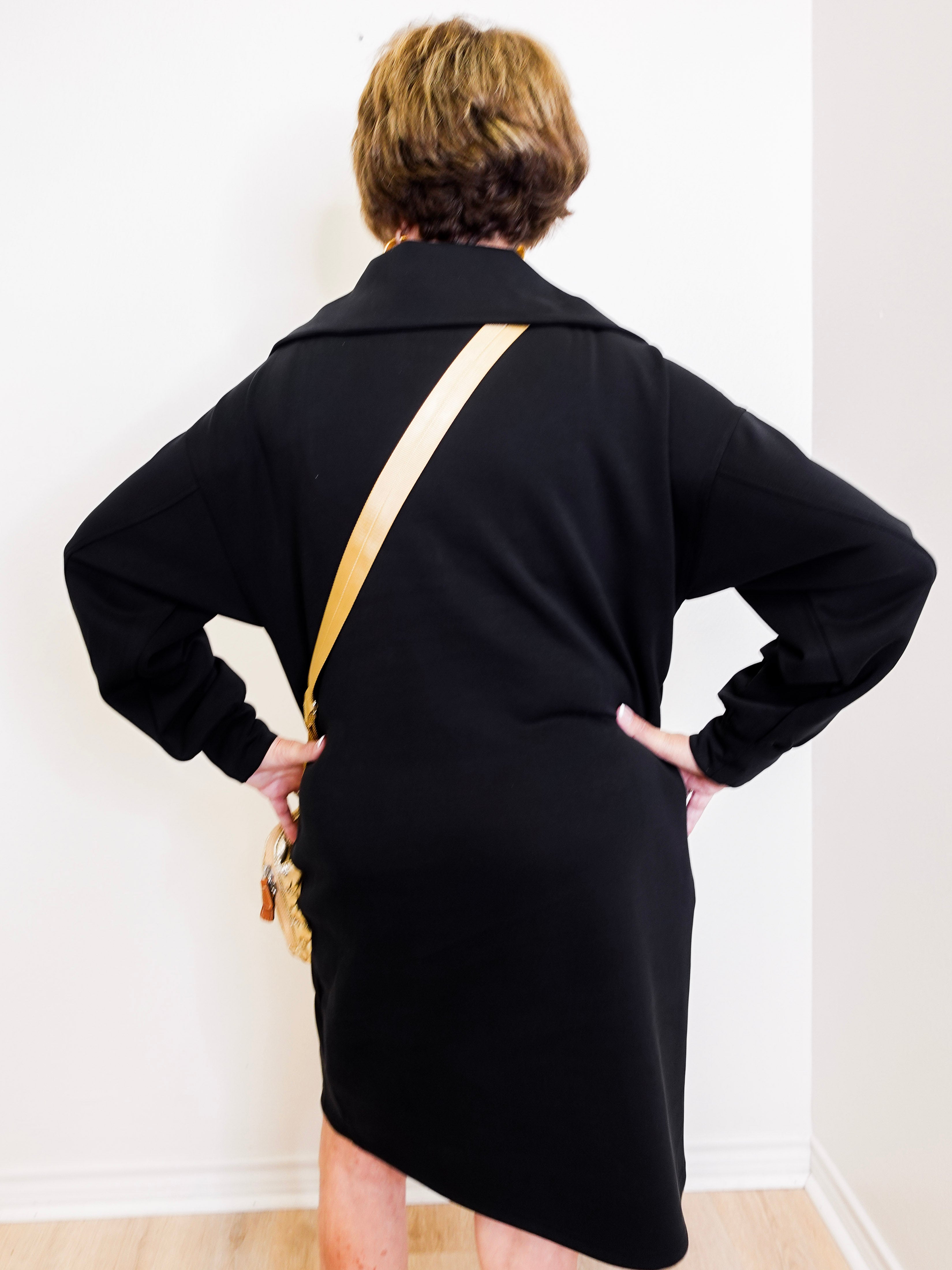 Person wearing a black dress with a gold strap over a white background