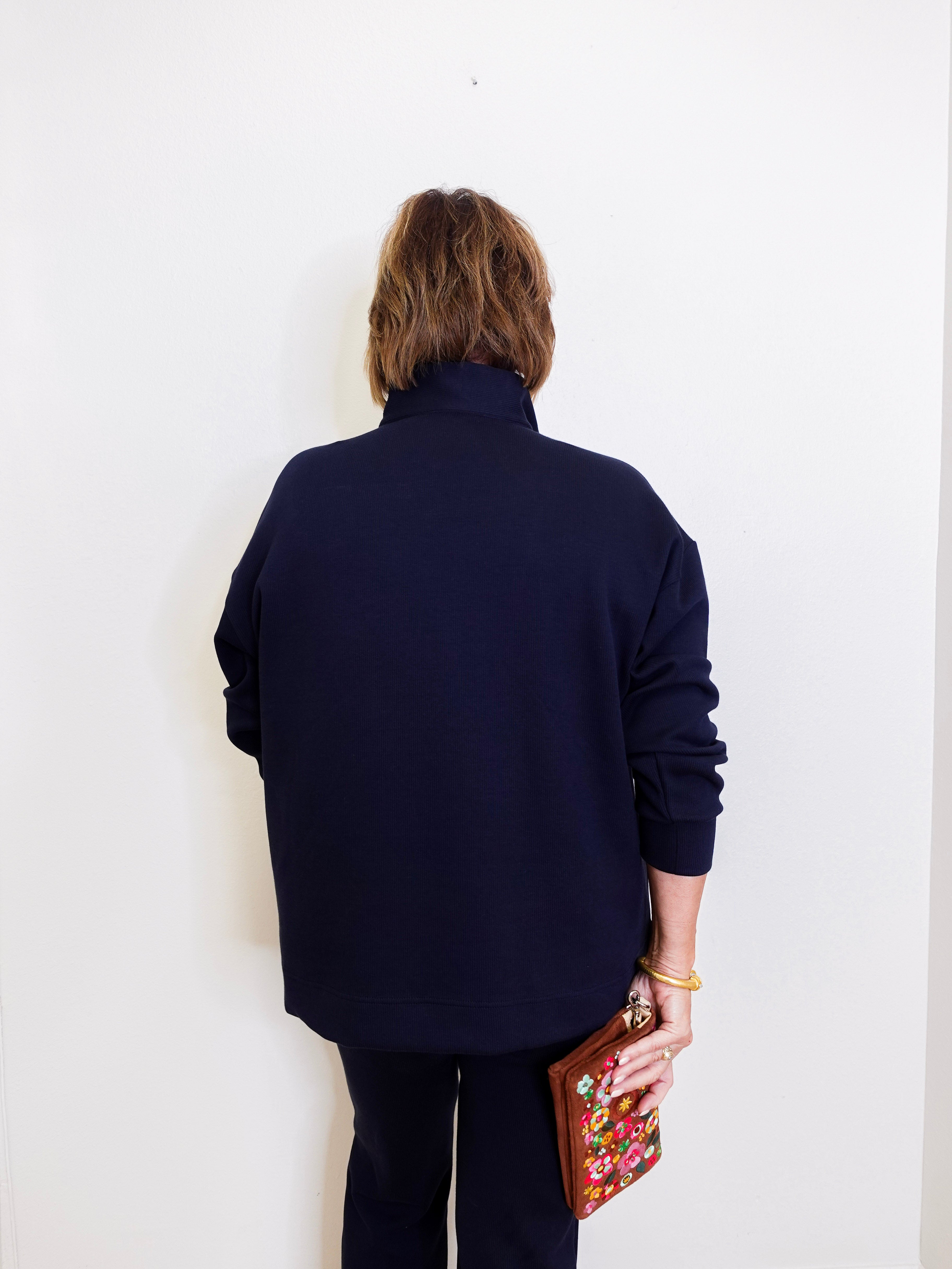 Person wearing a navy blue outfit holding a colorful clutch against a white background