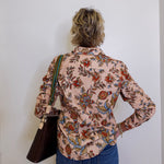 Person wearing a floral shirt and blue jeans against a white wall